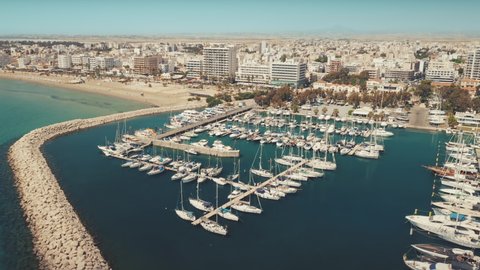 Aerial view yacht parking marina, Larnaca city center. Slow flight over modern harbor, dock for sailboats, zoom out. Travel destinations. Summer holidays, open border. Vacation on Cyprus island