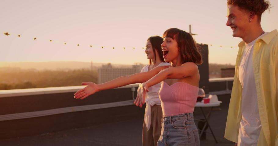 Cheerful young people feeling happy to meet together, hugging after long time of parting. Multiethnic friends students coming for rooftop party celebration at sunset. Reunion concept. Royalty-Free Stock Footage #1076354354