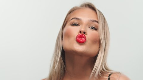 Beautiful Young Caucasian Woman Blowing a Kiss to the Camera with Gorgeous Red Lips and a Simple Make-Up Look in a White Background Set.
