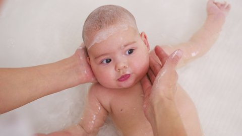 An adorable baby taking a bath with mother washing his head.
