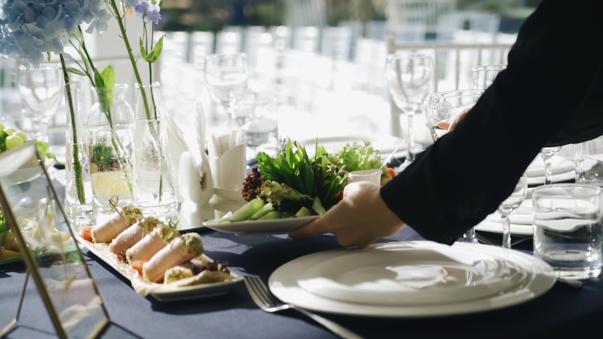 At the event, the waiter puts a plate of fresh delicious food on the table. Close-up of the table and his hands | Shutterstock HD Video #1076373506