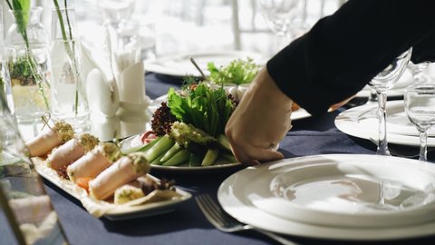 At the event, the waiter puts a plate of fresh delicious food on the table. Close-up of the table and his hands
