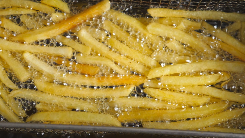 Close up of french fries is cooking into deep fryer. Crunchy potatoes is frying in hot boiling oil at cuisine. Process of making fast food at kitchen. Food preparing concept. Top view Slow motion Royalty-Free Stock Footage #1076375066