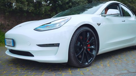 ROME, ITALY - APRIL 28, 2021: White electric Tesla car of premium class on test drive, electric car slowly passing along the cobblestone road showing the circle motion of black wheels. High tech