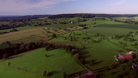 Dolly shot over the rolling hills with farms, farmlands, meadows with wooded banks natural fences, rural roads with blue and purple sky in South Limburg the Netherlands Aerial Drone View summer season