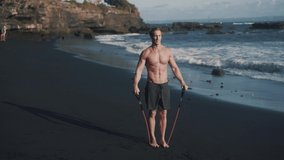 Front to side video of young sportsman doing exercises with elastic band. Caucasian fit guy flips his arms with resistance band outdoor workout. Concept of sportsman lifestyle. High quality 4k footage