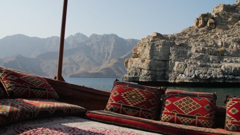Tracking shot of ocean and fjords from the POV of a traditional Dhow boat moving through the water with colorful geometric pillows on a clear sunny day in Khasab, Musandam Oman.
