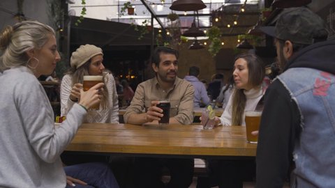 Bunch of friends drinking beer and raising a toast in a resturant. Mates doing cheers with beer glasses and celebrating an event at a bar meeting up.