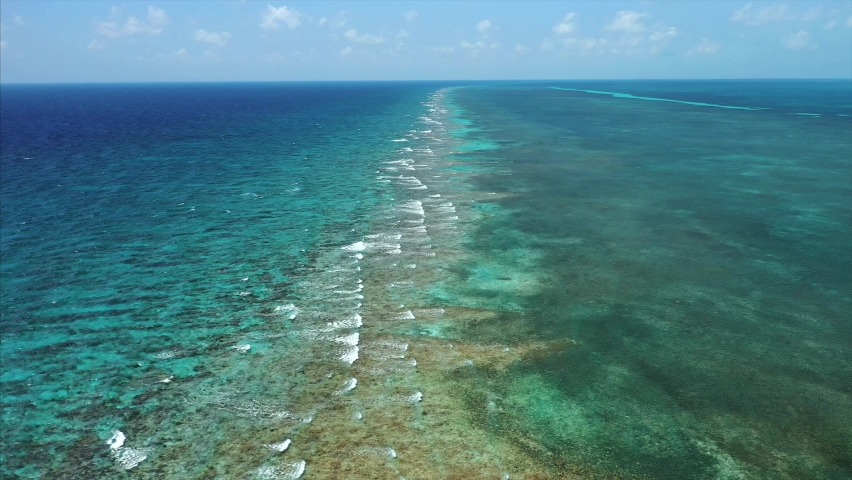 Aerial Drone flying over the Caribbean Barrier Reef in Belize. Waves crashing on coral. Shades of Blue. Royalty-Free Stock Footage #1076396567