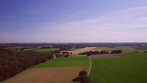 Aerial Landscape: Drone view of the countryside, farms, farmlands with harvests, rural roads and forests. Wind turbines on the horizon, Blue and purple sky in the background South Limburg Netherlands