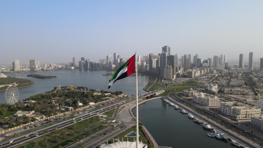 Aerial view of UAE flag and in background Sharjah skyline and Sharjah City Royalty-Free Stock Footage #1076414222
