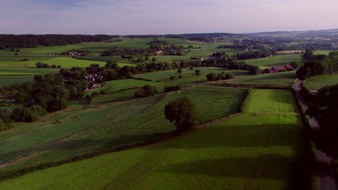 Aerial Drone View: South Limburg, Dutch valley landscape with rolling hills and farmlands, natural pastures, meadows and farms, with rural roads and forests. Blue and purple sky in the background