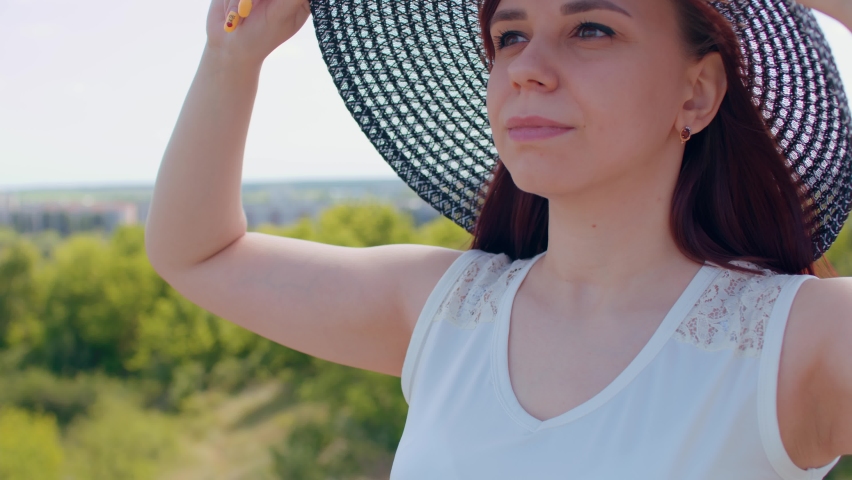 A beautiful woman in a white dress and an elegant hat poses against the background of nature. Beautiful elegant lady walking in the park wearing a hat and summer dress. Romantic image of a female