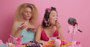 Mixed race women do makeup present beauty products record broadcasting live video talk to audience while apply lipstick and eyeshadow. Two famous female bloggers share content on social media