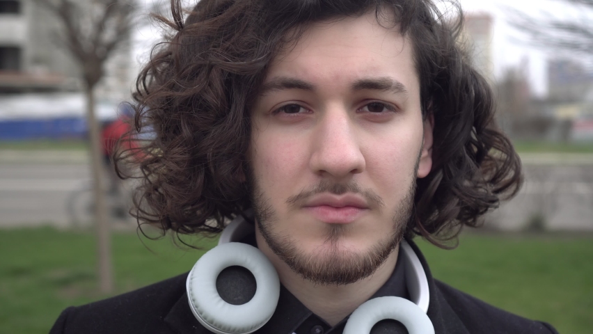 Portrait of a young curly haired brunette man. Close-up businessman or student outdoors