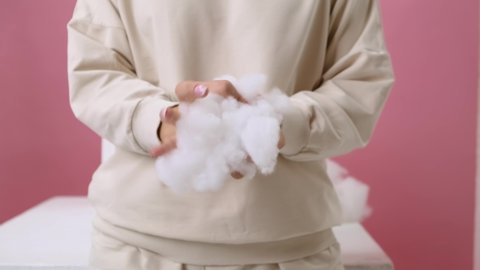 Medium shot. A girl in a vanilla-colored hoodie on a pink background and squeezes a voluminous artificial filler of white color