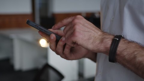 Close up view of a man's hands that hold black phone, looking for something