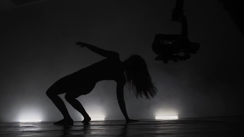 Modern ballet dancers performing together on dark stage. Silhouettes of performers and videographer recording the performance with smoke in the air.