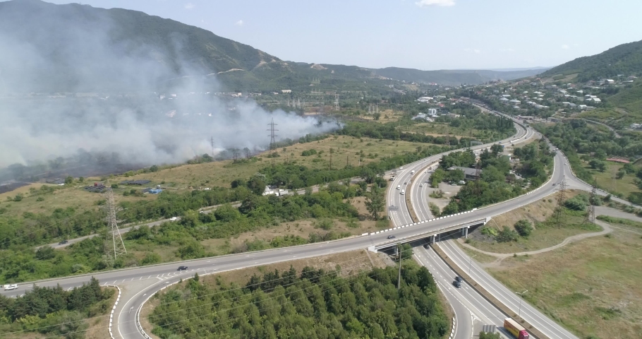 The dramatic view of destroying wildfire on wood near the highway, The hillside forest is in fire. Firefighting is involved in extinguishing a fire.