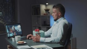 Multiracial man and woman making online video meeting to open the received presents from each other. Man calling from office, while woman from home.