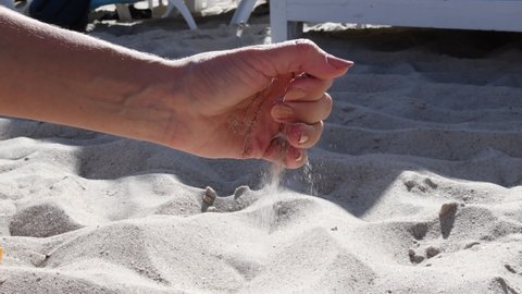 Woman hand pouring sand grains and then straighten and spread fingers of hand palm. Female hand playing with sand at sea beach in sunny summer day