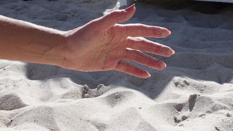 Sand grains fall from female handful then woman opens palm of hand with sand grains on skin. Young lady palm of hand playing with sand at sea beach in sunny summer day