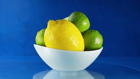 Whole and sliced lemons and limes in a white plate close-up rotate on a light blue background. 4k slow motion video.