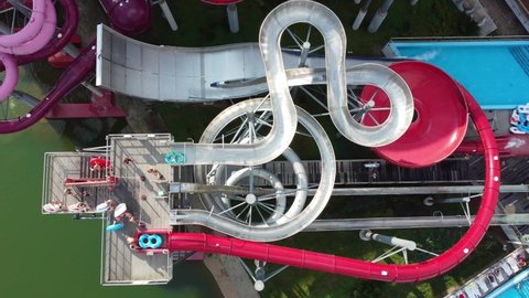 Aerial view of people descending from the water slide on inflatable rings at the water park. People having fun riding on slides in outdoor water park. High quality 4k footage