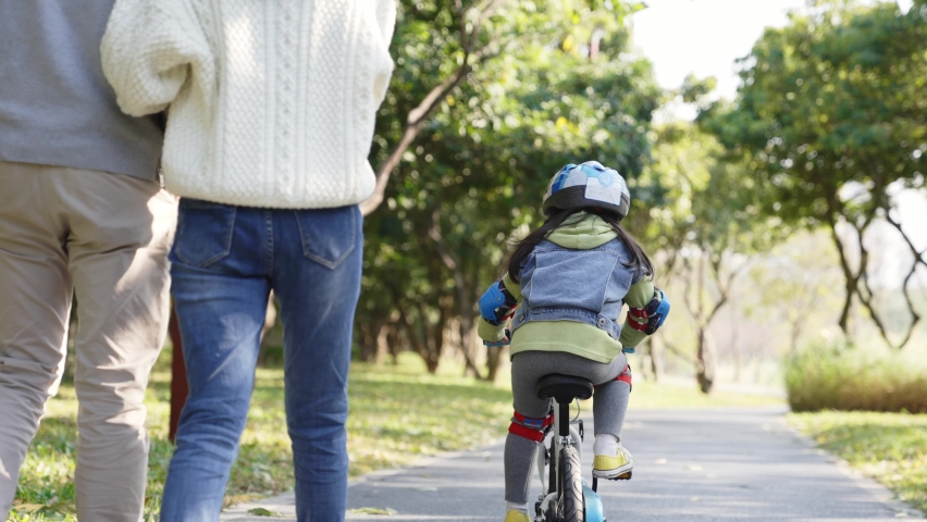 rear view of little asian girl riding bike with full protective gears outdoors in park while parents watching from behind Royalty-Free Stock Footage #1076468831