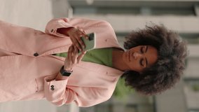 Vertical video. Serious young mixed race business woman using her smartphone while walking on the street. Urban technology and mobile typing communication concept