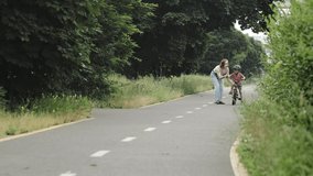 Mother teaching son to ride bicycle. Happy cute boy in helmet learn to riding a bike on the bike path in summer raining day . Family weekend. 4K video Slow motion.