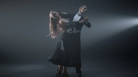 Full length of ballroom couple enjoying dance in spotlights background. Professional dancers performing waltz in dark background. Elegant man and woman dancing on stage. 