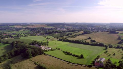 Aerial Drone View: Dutch valley landscape with roads, hills and farmlands, meadows and village landscape, with rural roads in South Limburg the Netherlands. Blue and purple sky in the background