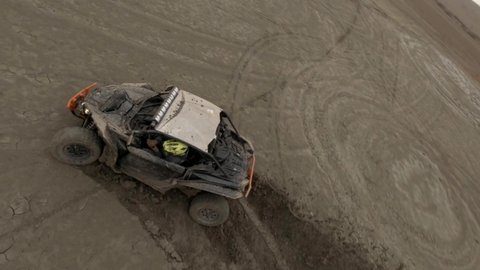 Brutal buggy automobiles drift on dried salt lake territory with brown sand leaving circle traces against hill silhouettes. Aerial view on sport fpv drone