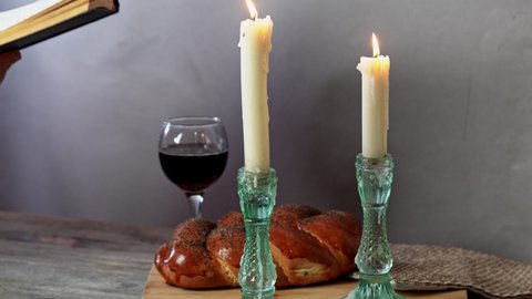 Shabbat Shalom. Challah bread, shabbat wine and candles on wooden table. A man reading a torah