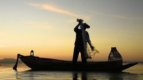 silhouette scene of Asian fisherman stay on a boat throwing fishing net caught fish for food in a river or lake with beautiful sunrise sky