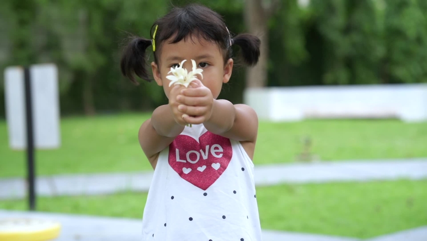 Adorable Asian little girl holding bouquet white flowers at garden.