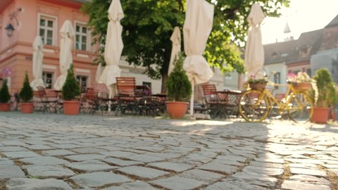 Street scene of medieval city Sighisoara Transilvania Romania. Slow steadicam shot. Cozy outdoor cafe at the morning. Camera focus at historic paving stone at foreground