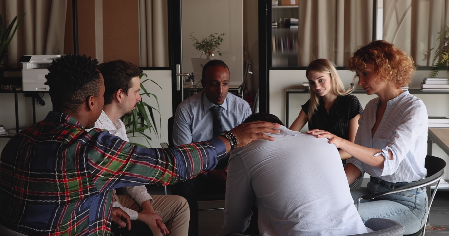 Diverse people sitting in circle supporting upset man at group therapy session. Colleagues calming unfairly dismissed teammate, stressful businessman getting psychological help, trust, support concept Royalty-Free Stock Footage #1076497886
