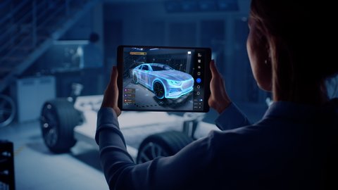 Automotive Engineer Working on Electric Car Chassis Platform, Using Tablet Computer with Augmented Reality 3D Software. Innovative Facility: Vehicle Frame with Wheels Becomes a VFX Virtual Model.