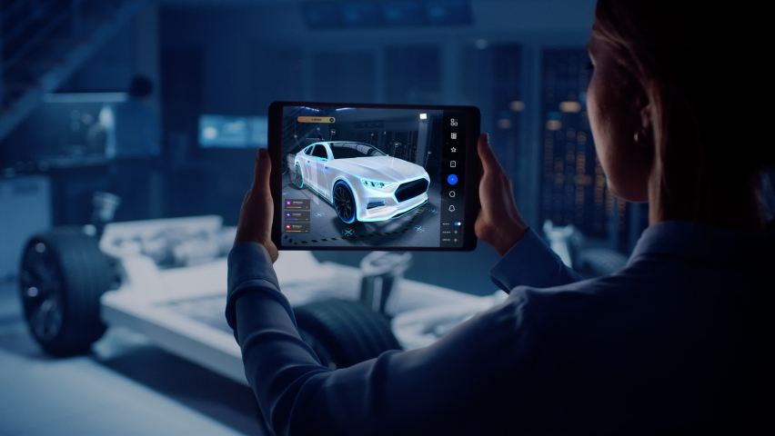 Automotive Engineer Working on Electric Car Chassis Platform, Using Tablet Computer with Augmented Reality 3D Software. Innovative Facility: Vehicle Frame with Wheels Becomes a VFX Virtual Model.