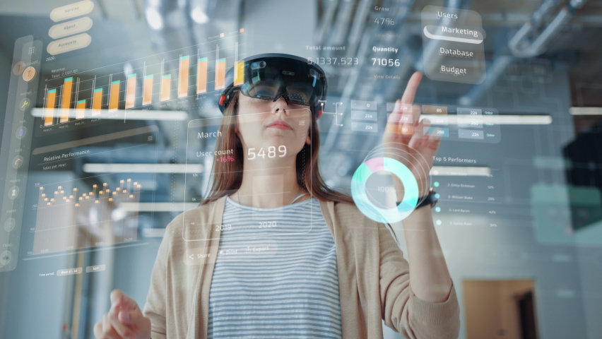 Young Adult Female Using Futuristic Augmented Reality Software Interface for Managing Business and Marketing Projects. Specialist in Office Wearing Headset to Look at VFX Animation with Financial Data | Shutterstock HD Video #1076498954