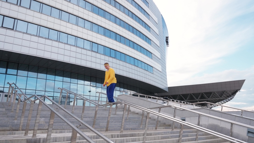 Parkour, young man performs a backflip over obstacles in the city and doing a flip on training area near modern buildings, 4k slow motion.