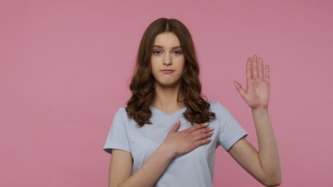 I swear! Sincere teenager girl with wavy hair raising hand to promise, taking vow with serious expression, giving oath to be faithful. Indoor studio shot isolated over pink background.