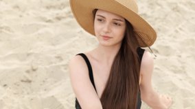 Portrait of a cute beautiful brunette girl in a hat on a background of sand on the beach. Relax near the water