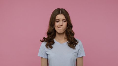 Adorable disappointed teenager girl in blue T-shirt holding fingers near forehead showing loser sign with sarcasm, unhappy because of crisis. Indoor studio shot isolated over pink background.