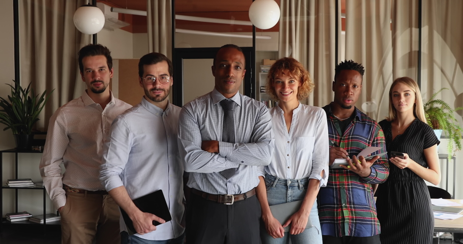 Six diverse multiracial professional business team portrait. Young company employees members led by African middle-aged boss standing in row in office pose on camera. Unity, career, equality concept Royalty-Free Stock Footage #1076517245