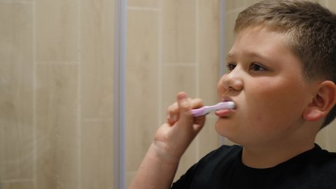 Little fat boy enjoying morning oral hygiene routine alone in bathroom close-up. Happy kid brushes teeth with toothbrush