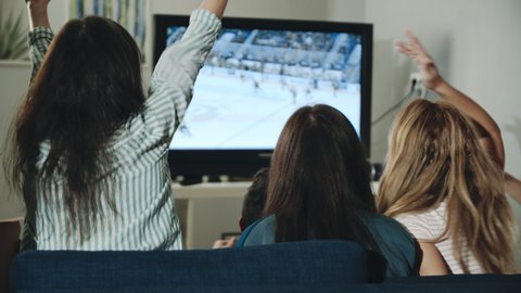 Backshot group of teens watching hockey match on tv celebrating goal. Excited millenials cheering for team sitting in living room. Concept of leisure, lifestyle, spending time together, victory.