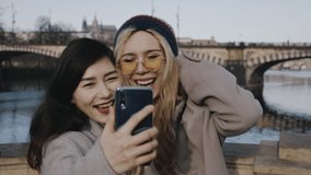 Close-up portrait of girls with smartphone or mobile phone in hands. Young pretty women photographing in front of background of city sights, taking selfie on beautiful place. Lifestyle concept.